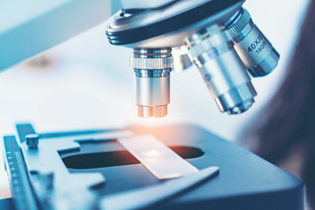 Scientist analyzing microscope slide at laboratory. Young woman technician is examining a histological sample, a biopsy in the laboratory of cancer research