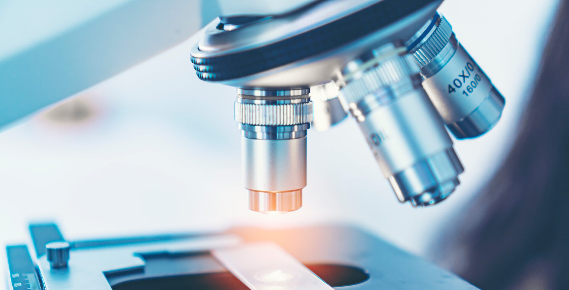 Scientist analyzing microscope slide at laboratory. Young woman technician is examining a histological sample, a biopsy in the laboratory of cancer research